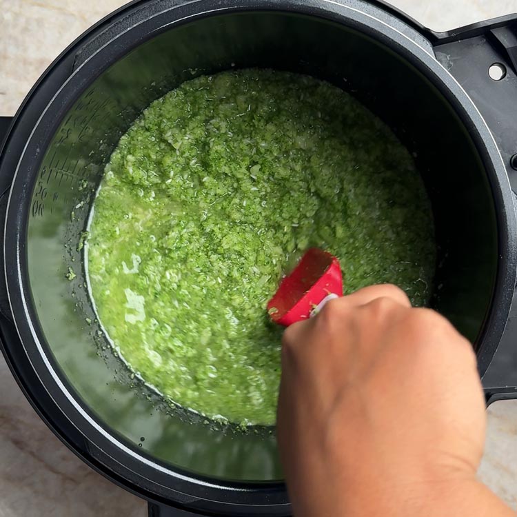 Hand stirring bright green broccoli and rice mixture with red spatula in pressure cooker