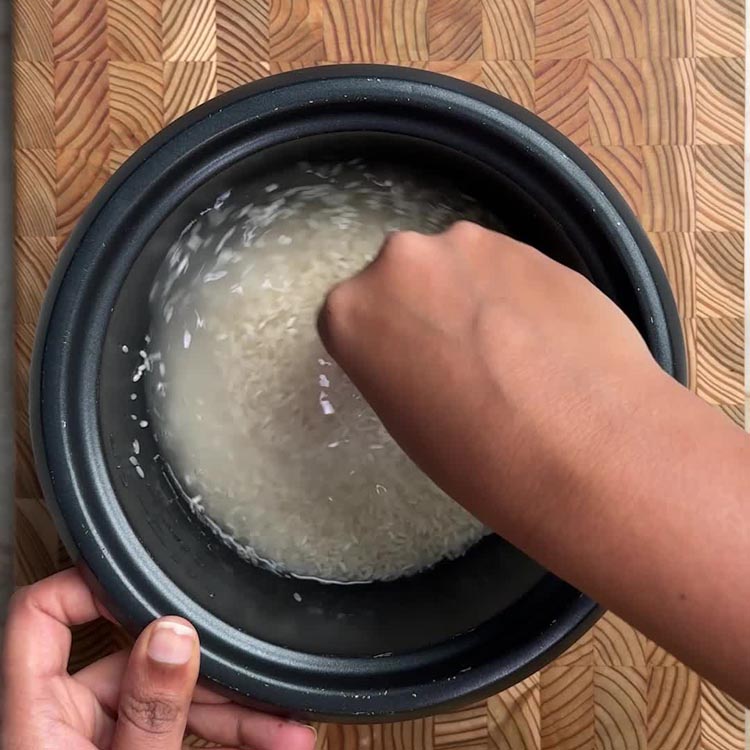 Hand rinsing white rice in dark rice cooker with running water to remove excess starch