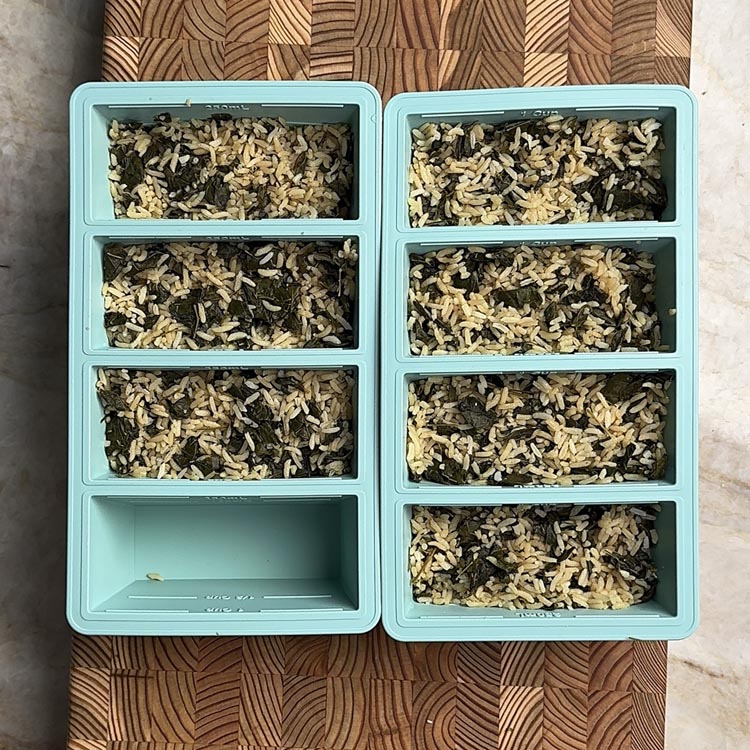 Seven portions of rice with moringa leaves divided in two turquoise meal prep containers on wooden board