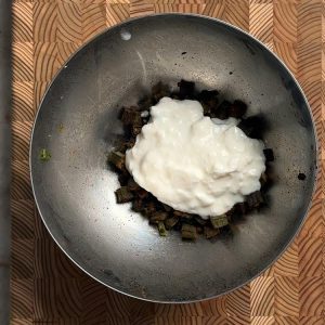 Crispy baked okra in a metal bowl topped with a dollop of white creamy yogurt