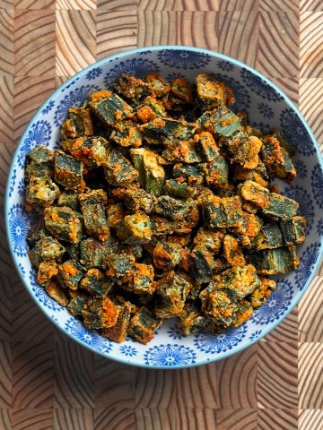Crispy baked besan okra with golden orange chickpea flour coating in blue and white decorative bowl