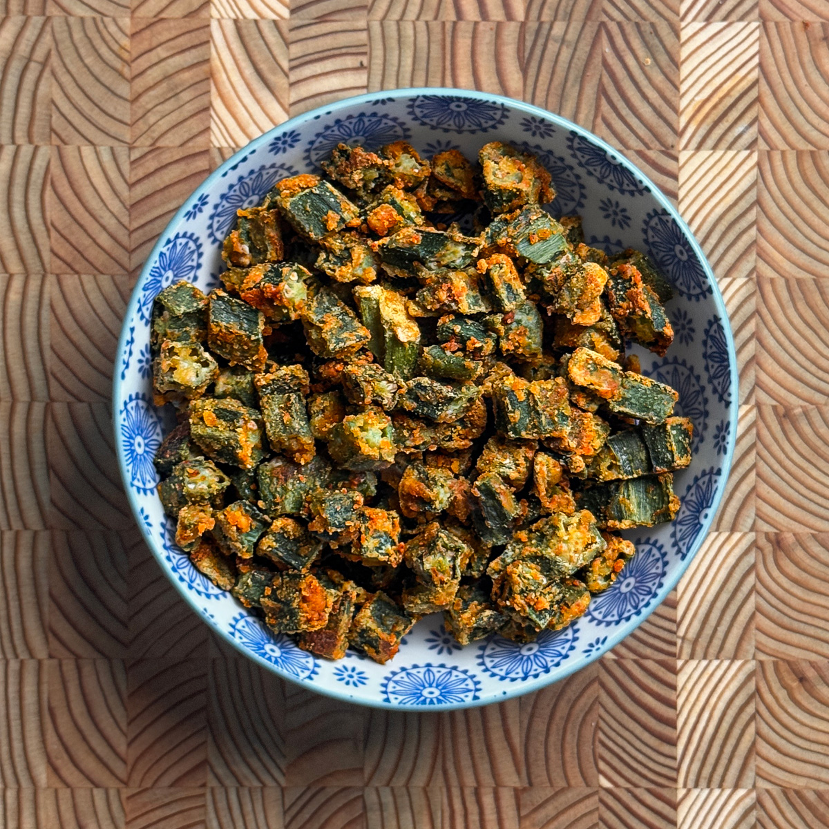 Crispy baked besan okra with golden orange chickpea flour coating in blue and white decorative bowl