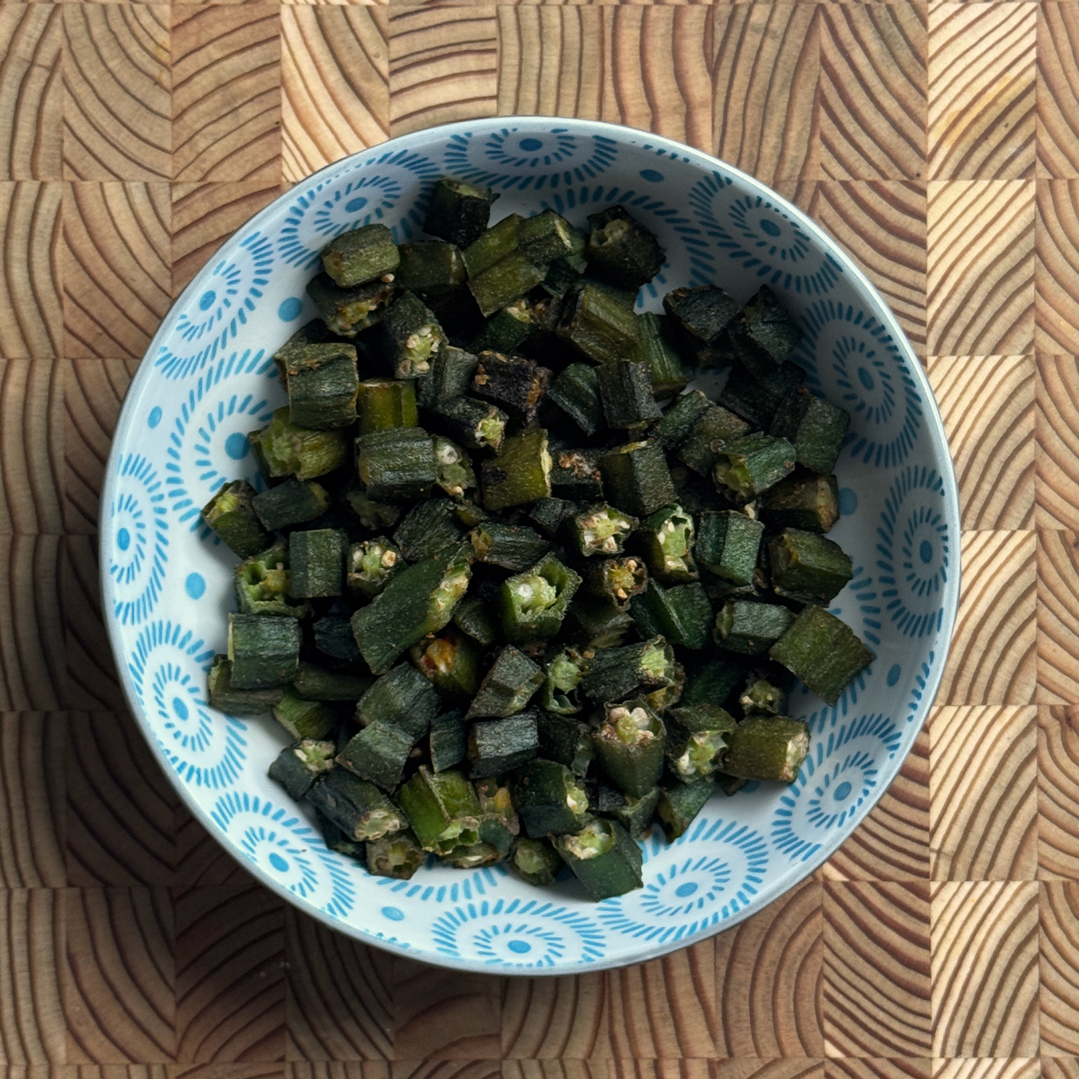 Crispy baked frozen okra in a blue and white patterned ceramic bowl on a wooden surface