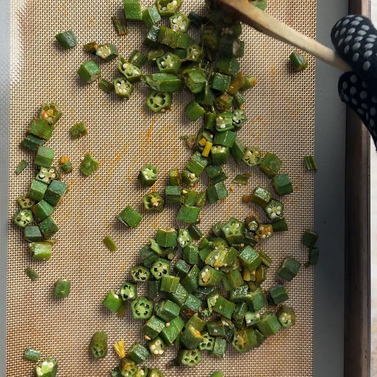 Okra pieces after 15 minutes of baking on a silicone mat with wooden spoon stirring