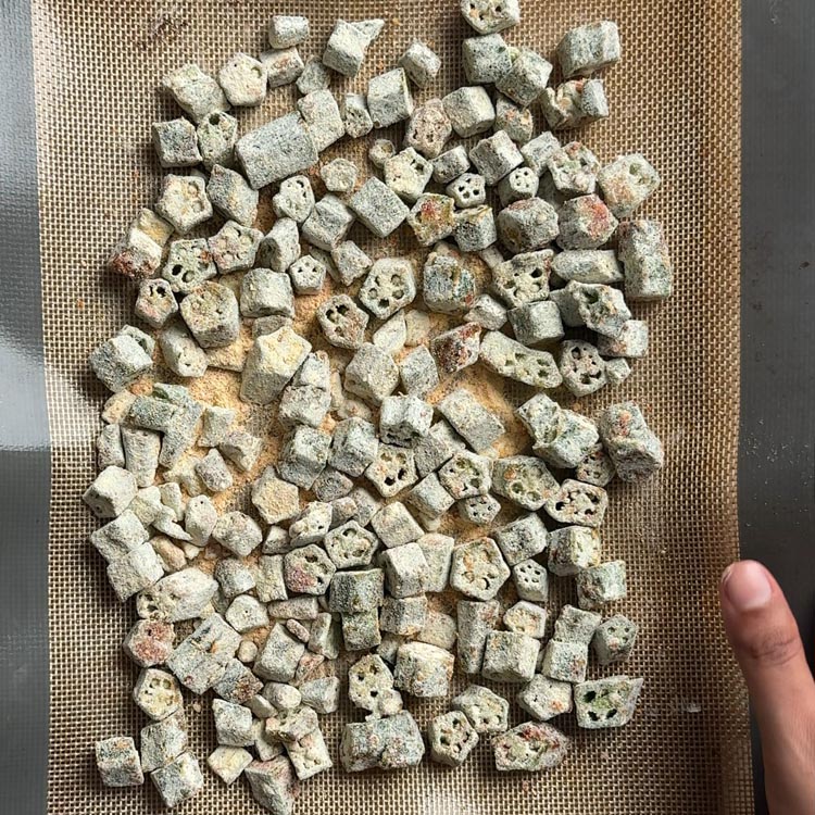 Besan coated okra pieces spread in single layer on silicone mat lined sheet pan before baking