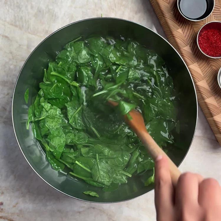 Stirring fresh spinach in hot water with a wooden spoon until wilted