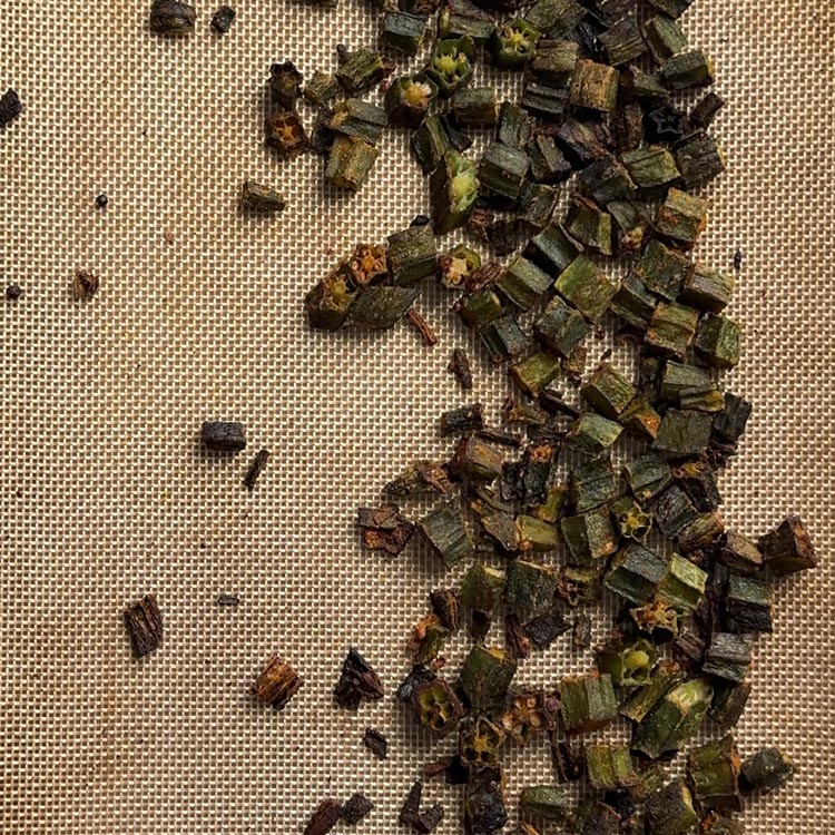 Fully baked crispy okra with golden brown edges spread on a silicone baking mat