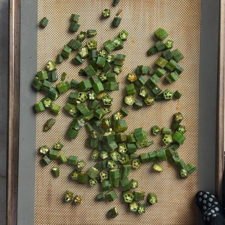 Okra pieces after 15 minutes of baking, showing early browning on a silicone mat