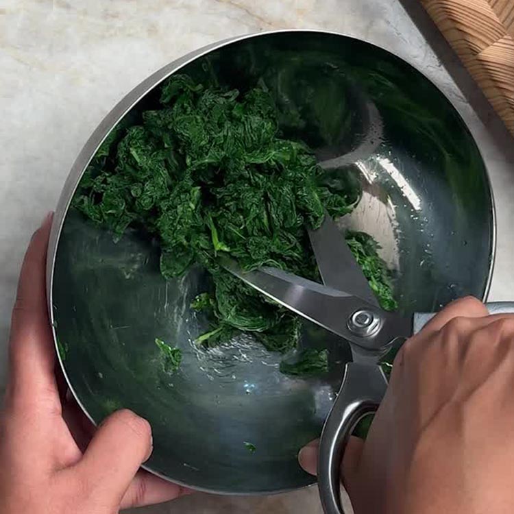 Using kitchen scissors to cut squeezed spinach into bite sized pieces