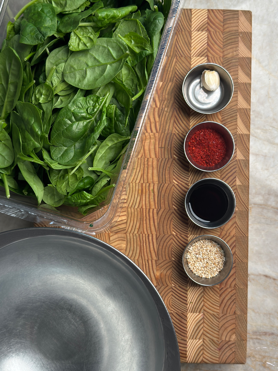Fresh baby spinach with garlic, gochugaru, soy sauce, and sesame seeds in small bowls