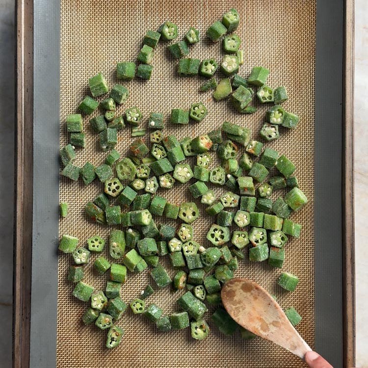 Green okra pieces arranged in a single layer on a silicone baking mat