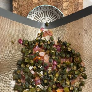 Crispy baked okra with roasted onions being transferred to serving bowl, golden brown and finished