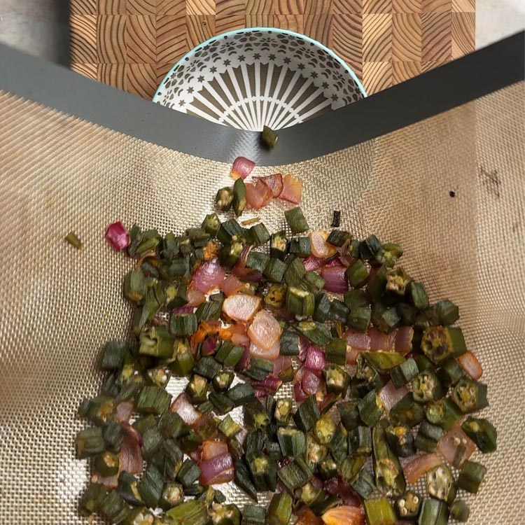 Crispy baked okra with roasted onions being transferred to serving bowl, golden brown and finished