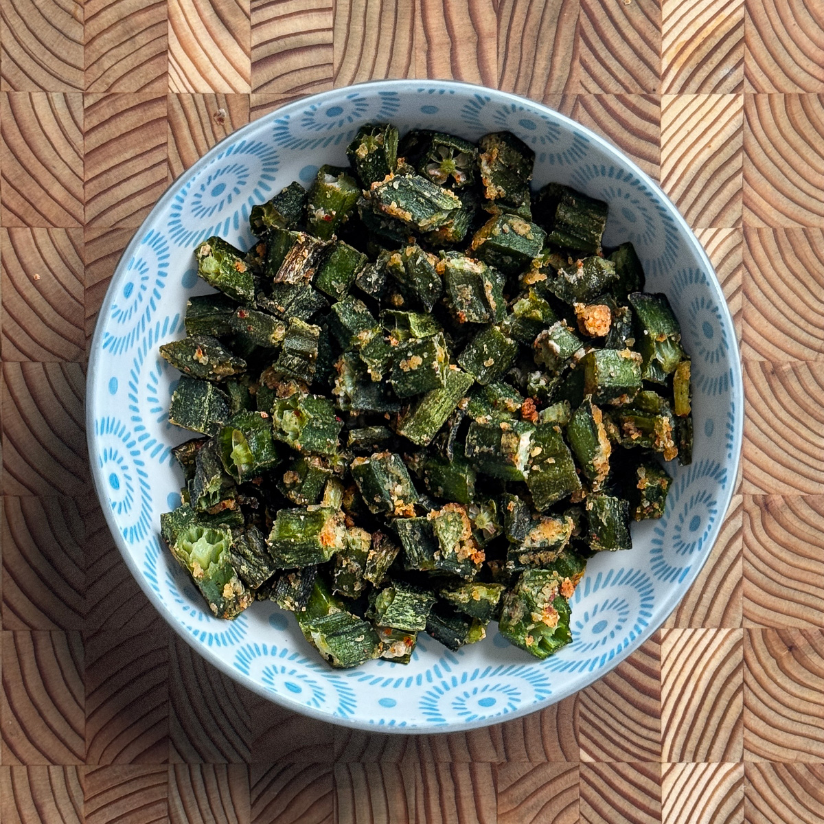 Crispy okra with garlic podi in blue and white decorative bowl with golden toasted coconut coating