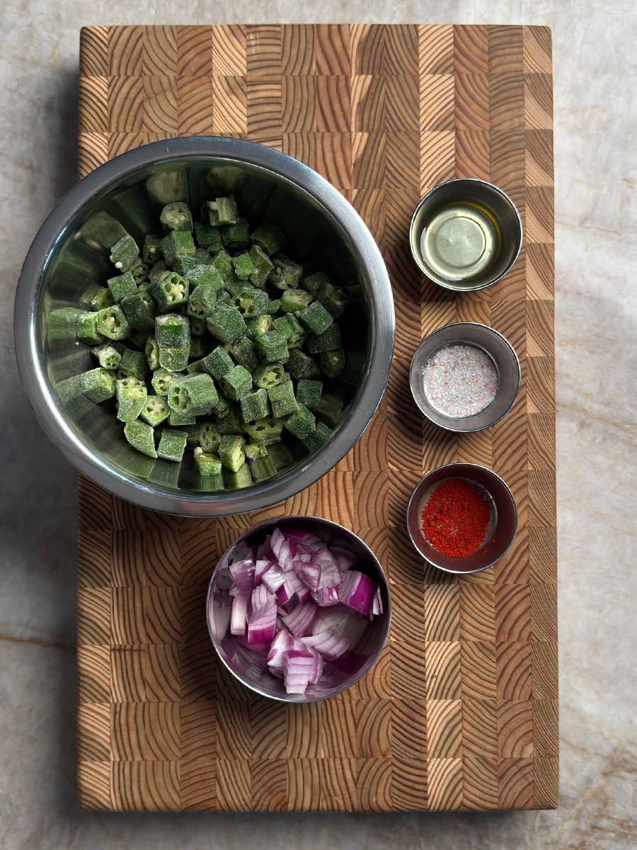 Frozen okra, sliced red onion, oil, salt and chili powder ingredients on cutting board for baked okra recipe