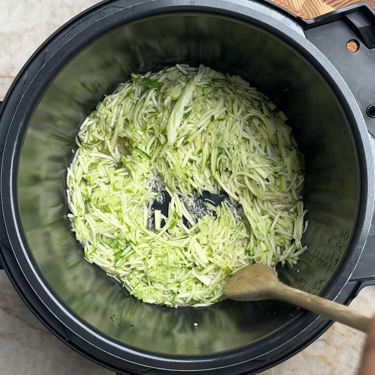 Mound of shredded zucchini over rice in a rice cooker pot with a wooden spoon