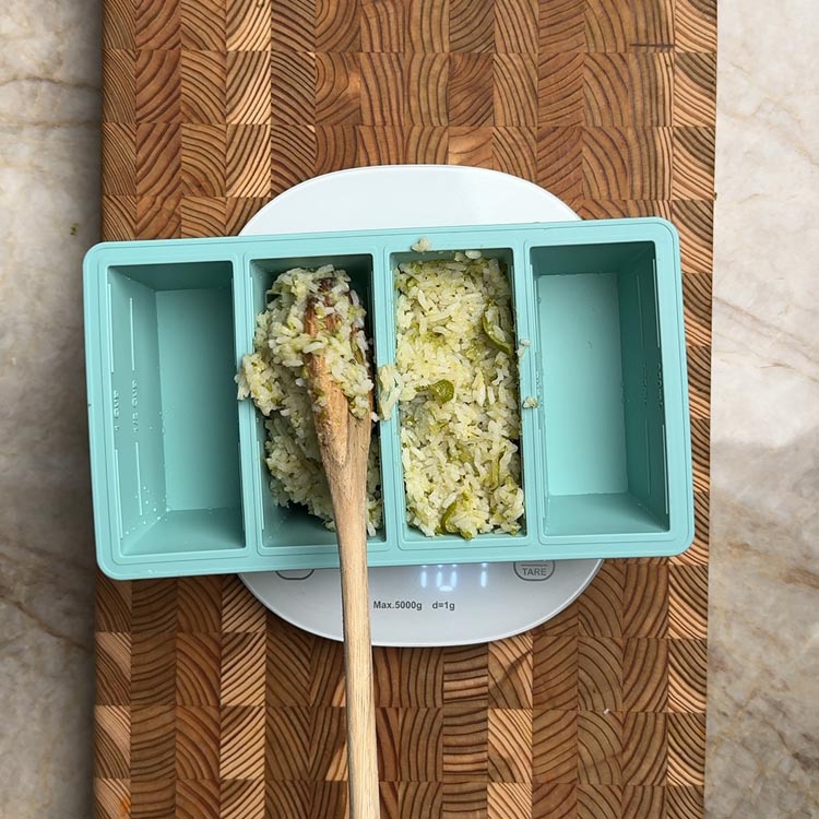 Spooning cooked rice into teal silicone freezer tray on kitchen scale