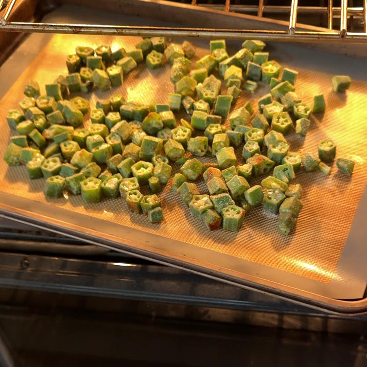 Seasoned okra roasting on a silicone mat inside a hot oven with golden lighting