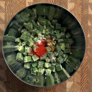 Cut frozen okra pieces topped with red chili powder and salt in a stainless steel mixing bowl