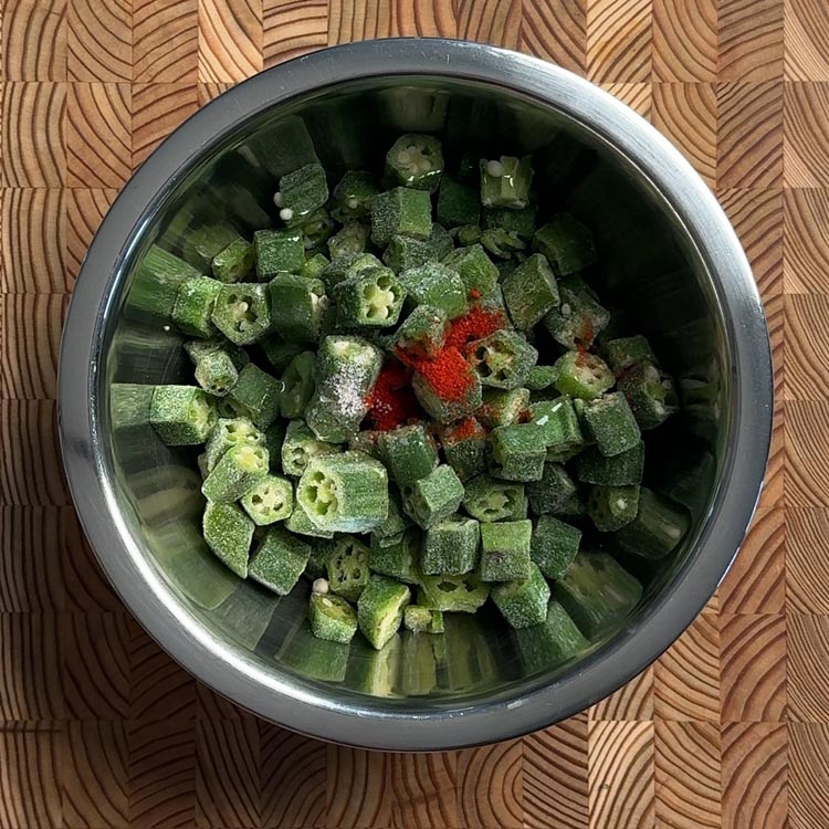 Cut okra pieces tossed with red chili powder and salt in a stainless steel mixing bowl