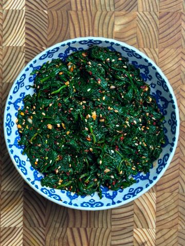 Spicy Korean spinach side dish topped with sesame seeds in a blue patterned bowl