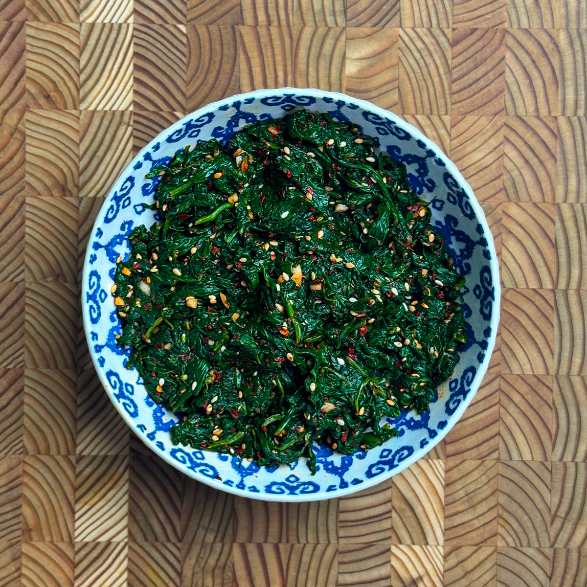 Spicy Korean spinach side dish topped with sesame seeds in a blue patterned bowl