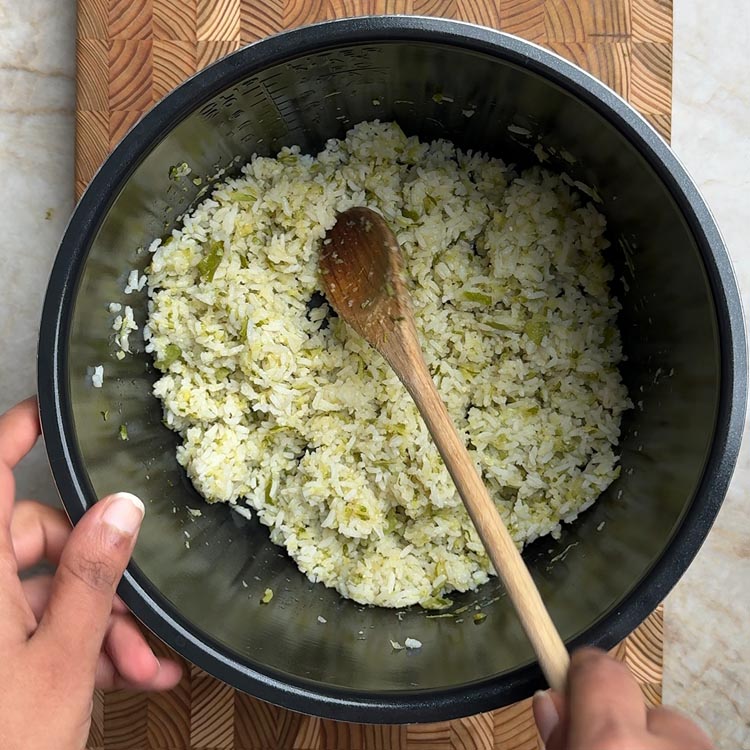 Cooked zucchini rice being fluffed with a wooden spoon in a rice cooker, showing fluffy texture
