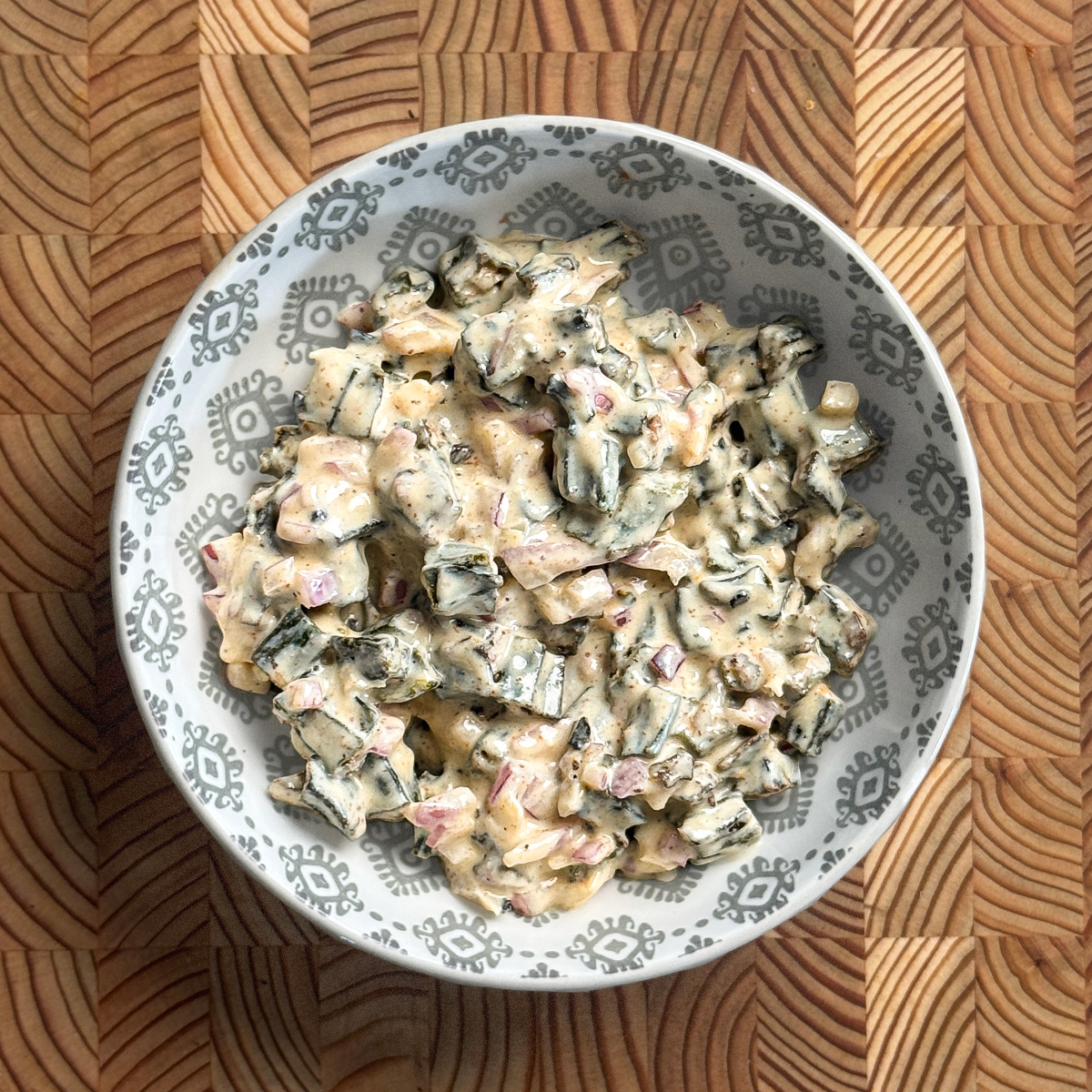 Creamy yogurt okra with diced red onions in a decorative gray and white patterned bowl