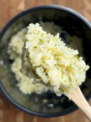 Fluffy zucchini rice with visible green flecks lifted on a wooden spoon from a dark bowl