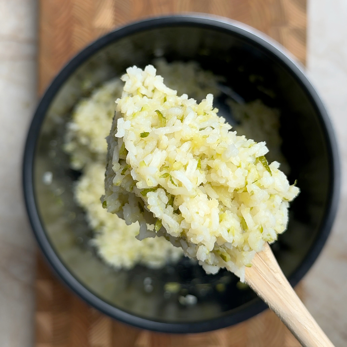 Fluffy zucchini rice with visible green flecks lifted on a wooden spoon from a dark bowl
