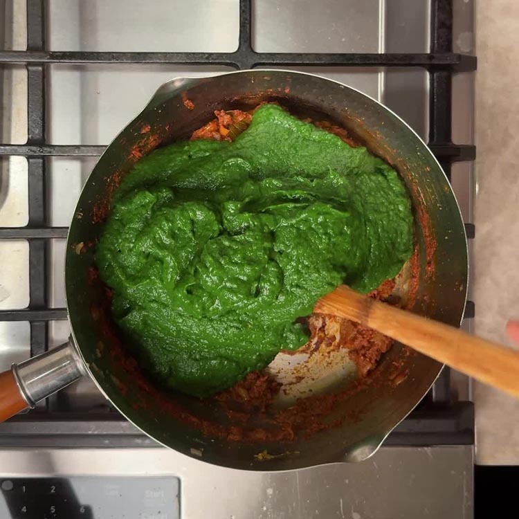 Bright green spinach broccoli puree added to spiced onion tomato base in pan