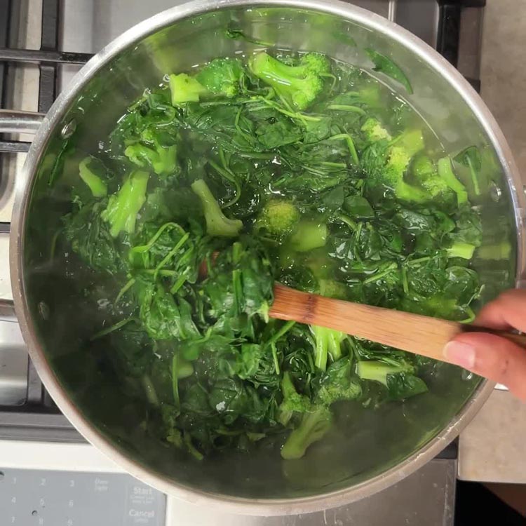 Fresh spinach and broccoli blanching together in pot with wooden spoon stirring