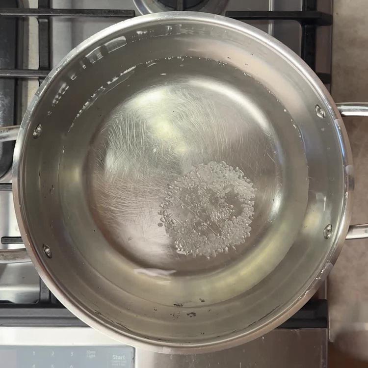 Salted water beginning to boil in a stainless steel pot on gas stovetop