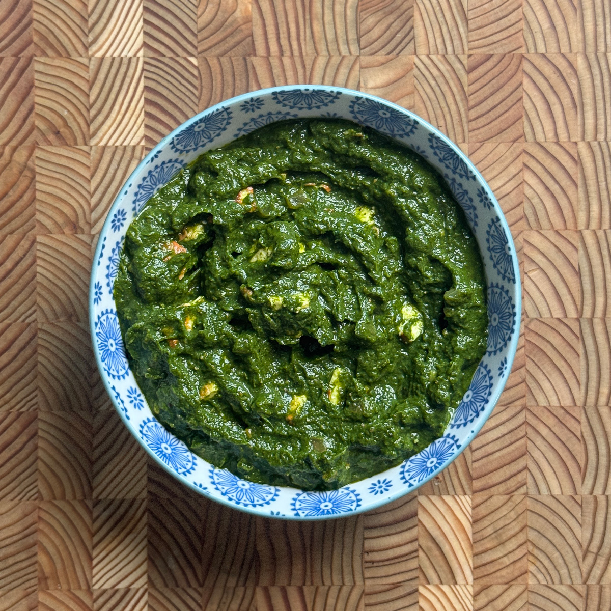 Creamy green broccoli palak paneer curry in a blue and white ceramic bowl on wooden board