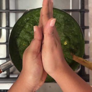 Hands crushing dried kasuri methi between palms over the finished palak paneer