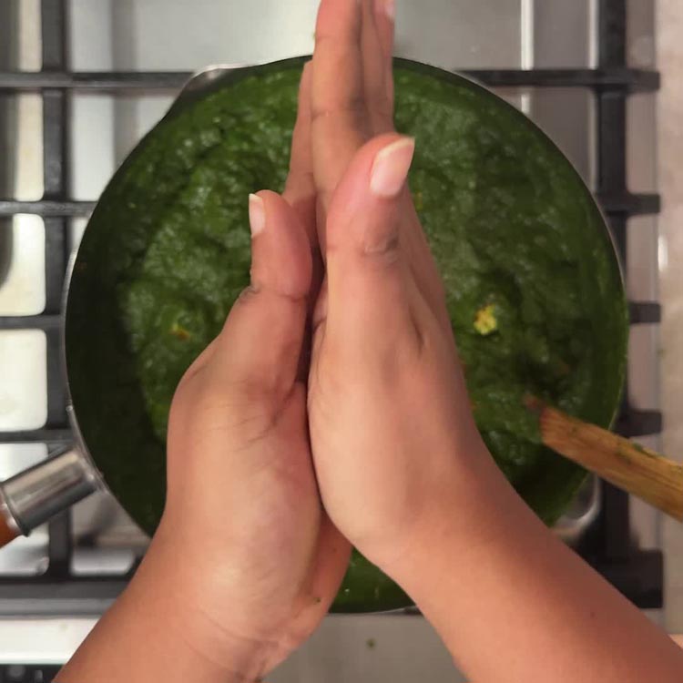 Hands crushing dried kasuri methi between palms over the finished palak paneer