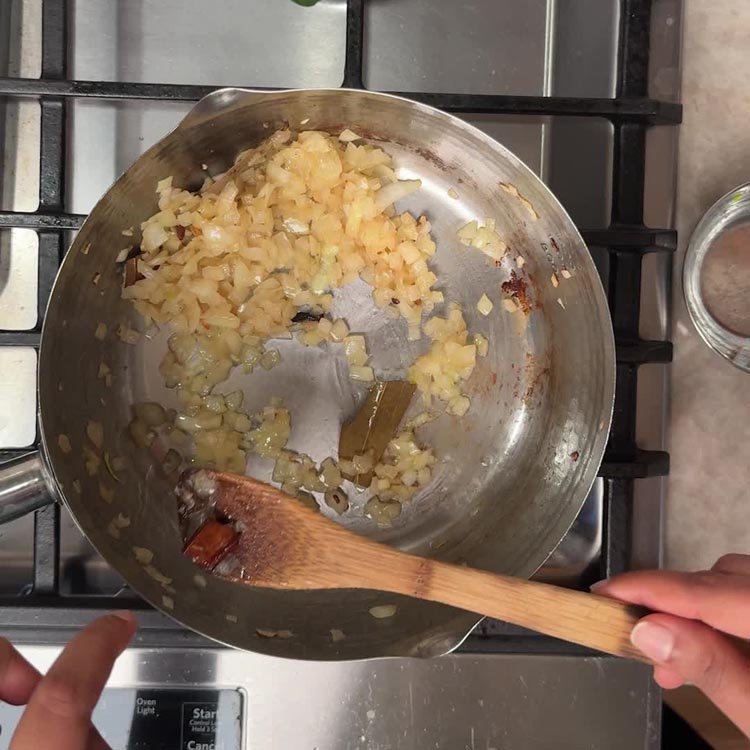 Chopped onions frying until golden brown with bay leaf in stainless steel pan