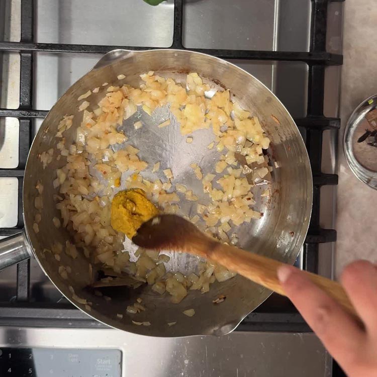 Ginger garlic paste added to golden onions in pan with wooden spoon stirring
