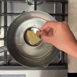 Bay leaf, cinnamon stick, and cloves being added to hot oil in stainless steel pan
