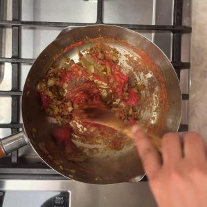 Tomato passata and spice powders cooking with onions in stainless steel pan