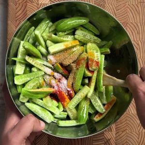 Tossing sliced dondakaya with turmeric, chili, and coriander in a mixing bowl