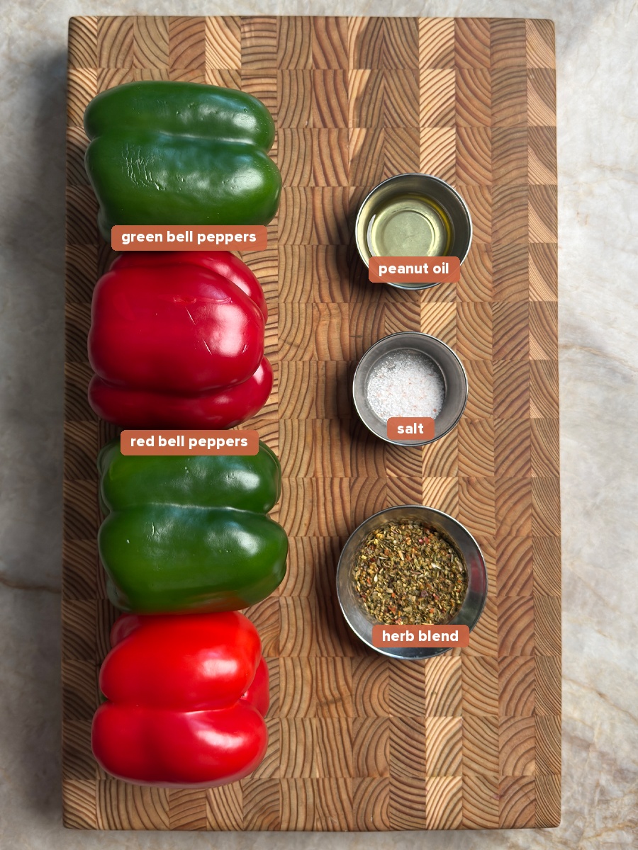 Two green and two red bell peppers with peanut oil, sea salt, and herb blend on a wooden cutting board