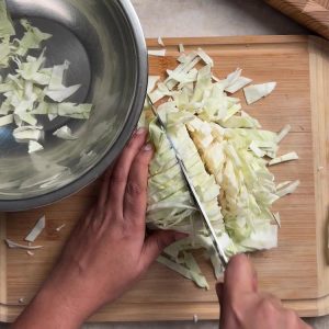 Hands chopping fresh green cabbage into bite sized pieces on a wooden cutting board