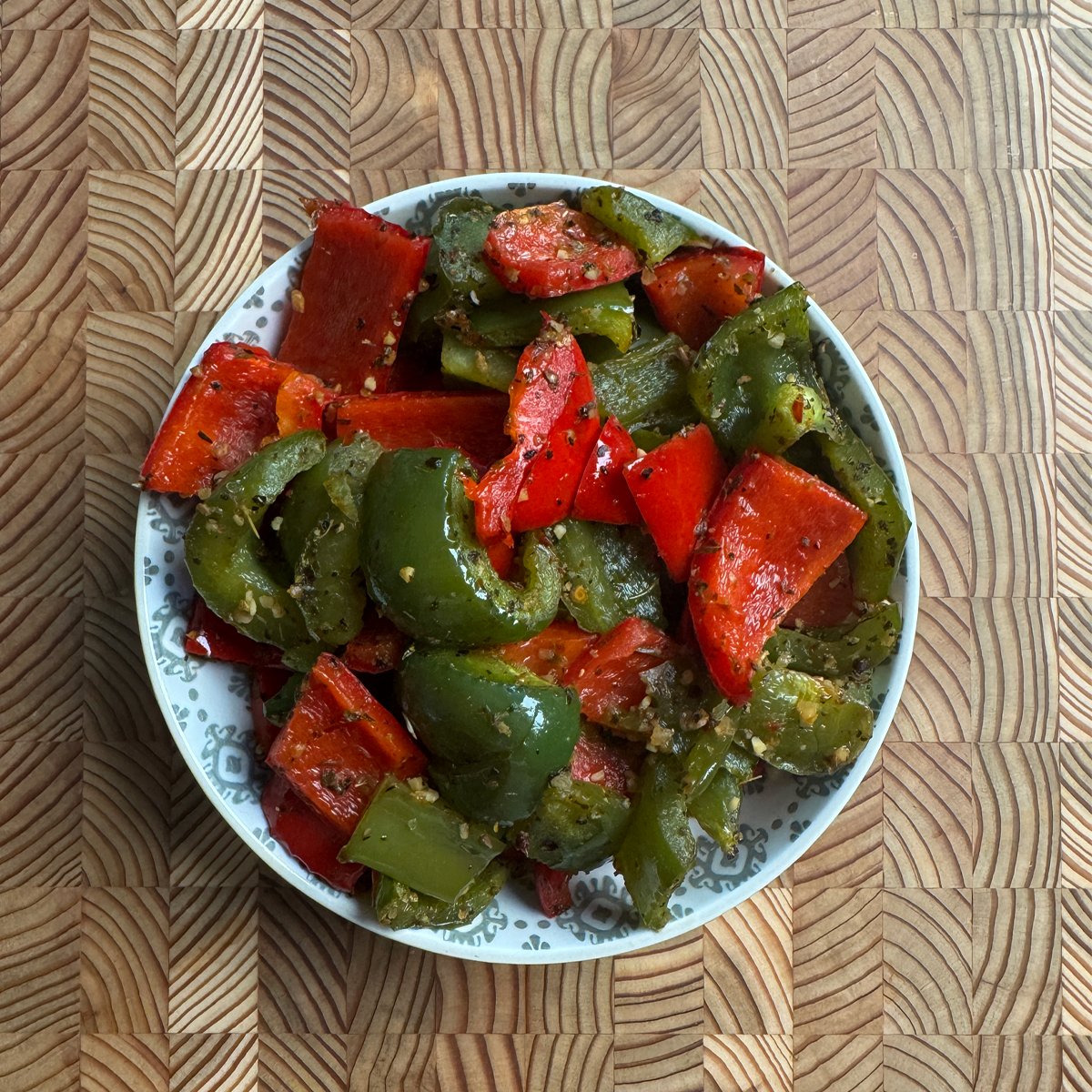 Oven roasted bell peppers served in a decorative bowl, overhead view, hands holding the bowl