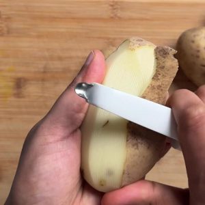 Hands peeling a russet potato with a vegetable peeler on a cutting board