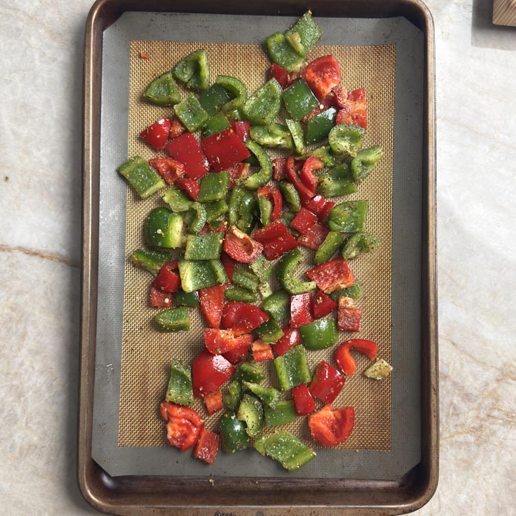 Seasoned raw bell pepper chunks spread in a single layer on a silicone lined baking sheet