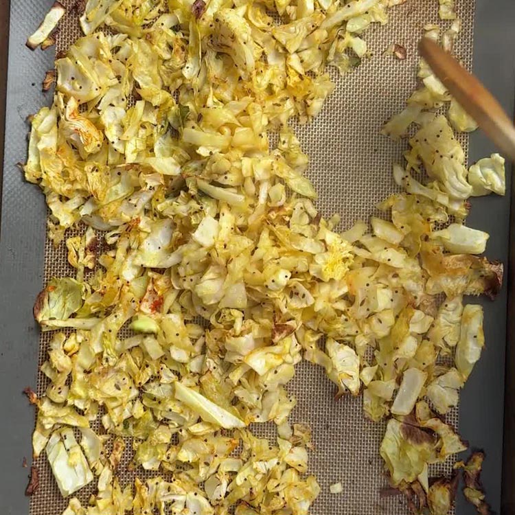 Golden roasted cabbage spread on a silicone lined baking sheet with visible crispy edges