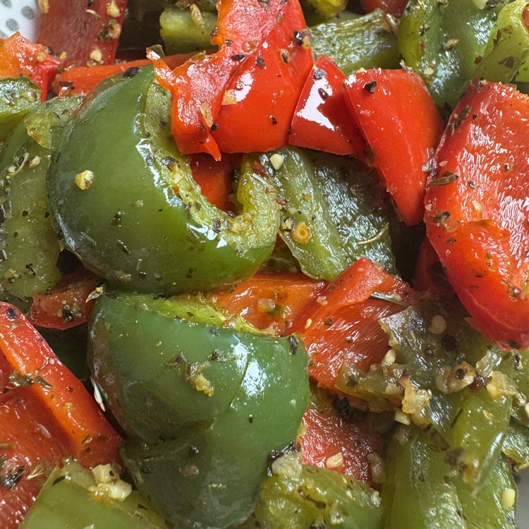 Close up of glossy roasted green and red bell peppers with charred edges and herb seasoning