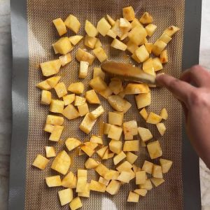 Spreading seasoned potato cubes in a single layer on a lined baking sheet with a spatula