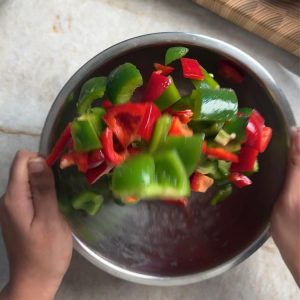 Tossing cut bell peppers in a stainless steel mixing bowl to coat with oil